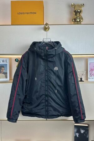 Close-up of a black Moncler hooded nylon windbreaker jacket with red and blue piping stripes running down the shoulders and sleeves. It features a Moncler logo on the chest.