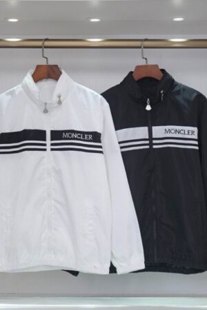 A pair of technical windbreakers in black and white, featuring bold horizontal chest stripes and signature branding hanging on a clothing rack