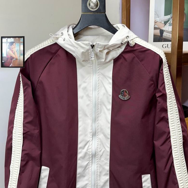 Front view of a burgundy and white hooded windbreaker jacket with sleeve stripes and a chest logo, hanging in a luxury retail setting.
