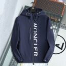 Navy blue hooded windbreaker jacket with white vertical lettering on the front, hanging on a black hanger against a modern interior background.