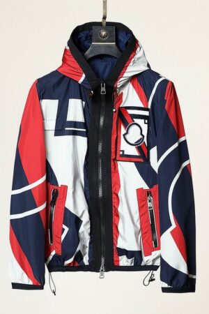 A lightweight, hooded windbreaker jacket with a bold, abstract geometric pattern in red, white, and navy blue. It has a black full zip and a circular logo patch on the left chest.