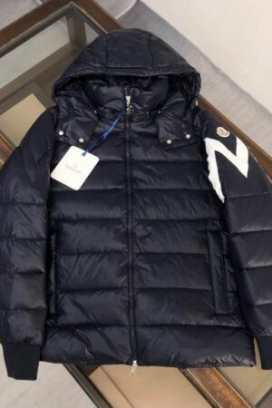 A white hooded puffer jacket with horizontal quilting, featuring a large black chevron graphic on the sleeve and a small logo patch on the other shoulder.