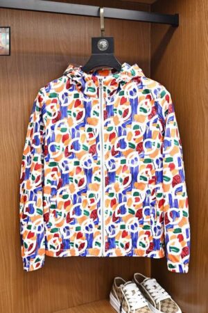 A vibrant, multi-colored men's windbreaker featuring an abstract graffiti print in orange, blue, and white, hanging in a wooden wardrobe.