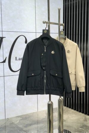 A black and a cream bomber jacket hanging on a silver rack, featuring a unique asymmetrical front flap and large square pockets.