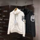 Two hooded Moncler style windbreaker jackets hanging on display, one in white and one in black, both featuring a large, distinctive logo graphic patch on the left sleeve.
