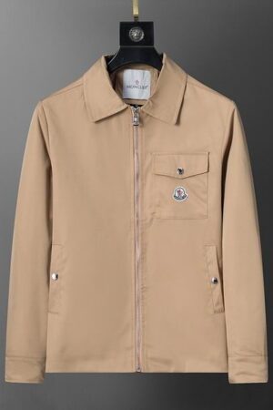 A front-facing view of a beige men's zip-up jacket with a pointed collar, a chest flap pocket, and a logo patch, hanging against a grey gradient background