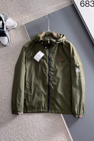 An olive green hooded windbreaker jacket with a full front zipper and a tactical arm pocket, featuring a signature designer-style logo on the chest and arm.