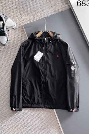 A sleek black technical hooded jacket with a full-length zipper and a tactical pocket on the left arm, featuring a small red designer-style logo on the chest.