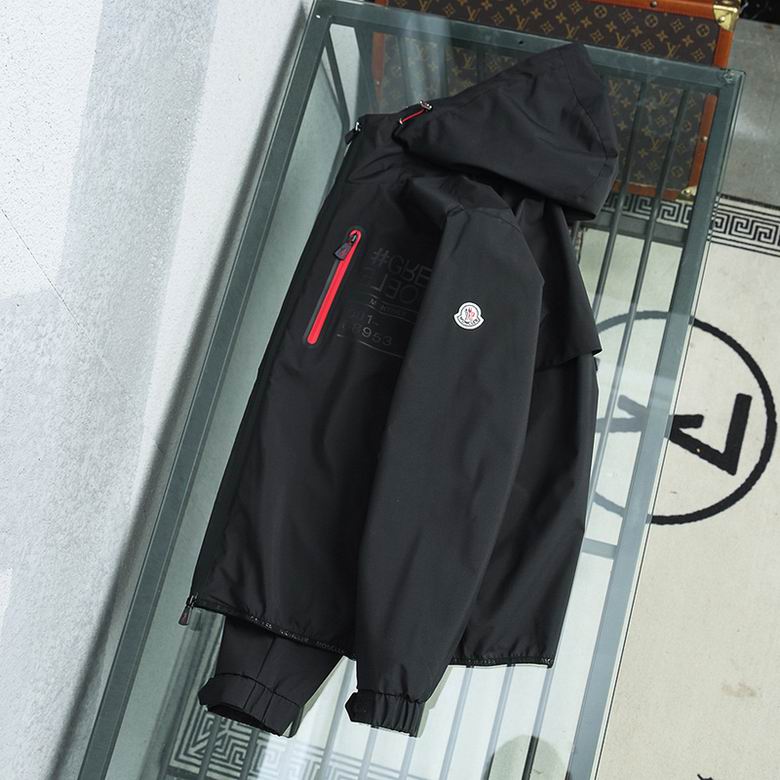 A high-performance black shell jacket featuring dual red-trimmed chest zippers and an integrated protective hood.