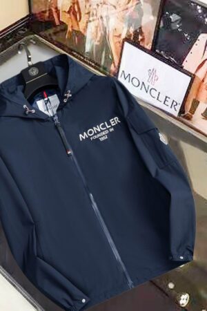 Black Moncler-style hooded jacket with "Founded in 1952" text on the chest and a utility pocket with a logo patch on the sleeve.